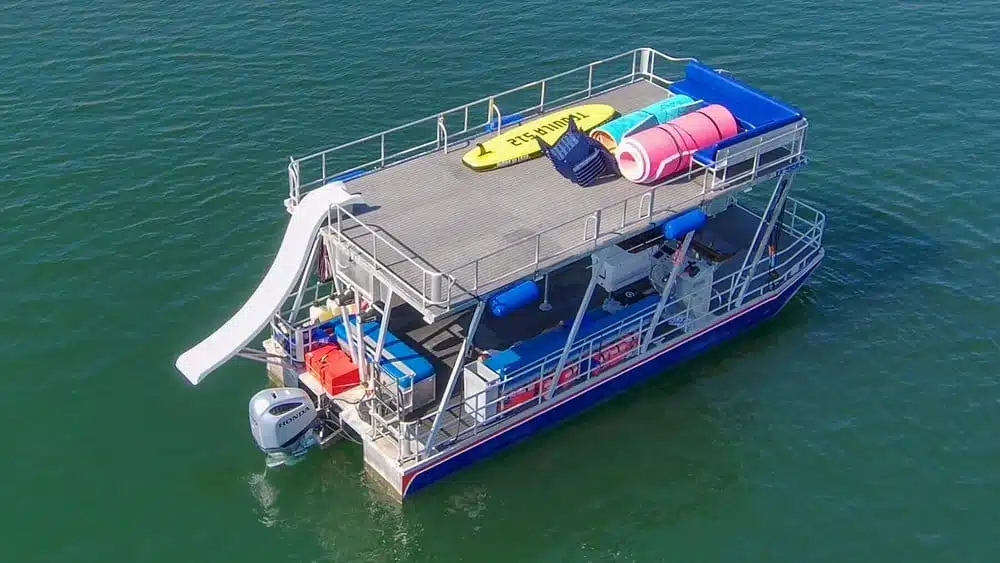 Double-deck pontoon party barge with slide and water toys anchored on the lake.