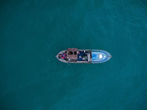 Aerial view of small fishing boat floating alone on deep blue water.