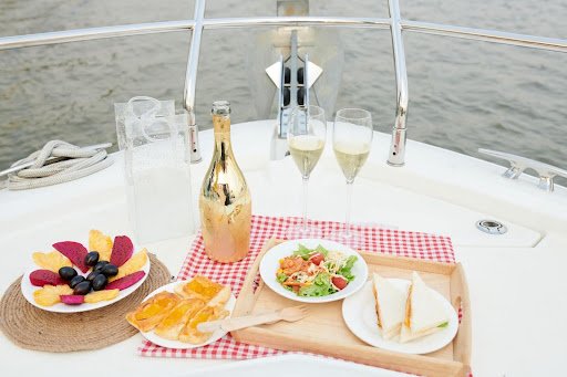 Luxury boat table set with champagne, glasses, fresh salad, fruit, and sandwiches.